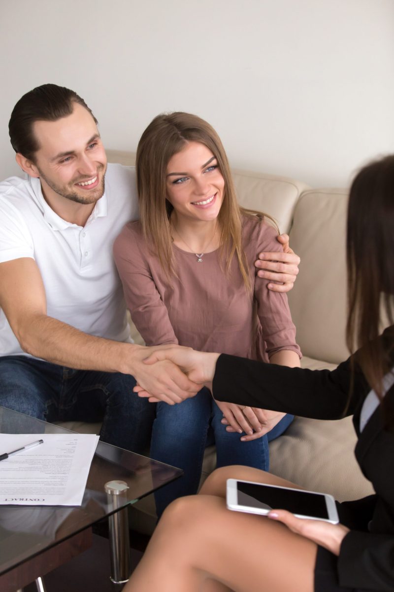 Happy cheerful couple shaking hands with female travel manager or bank worker after signing contract, personal insurance agreement, deal with advisor, lawyer or consultant, vertical